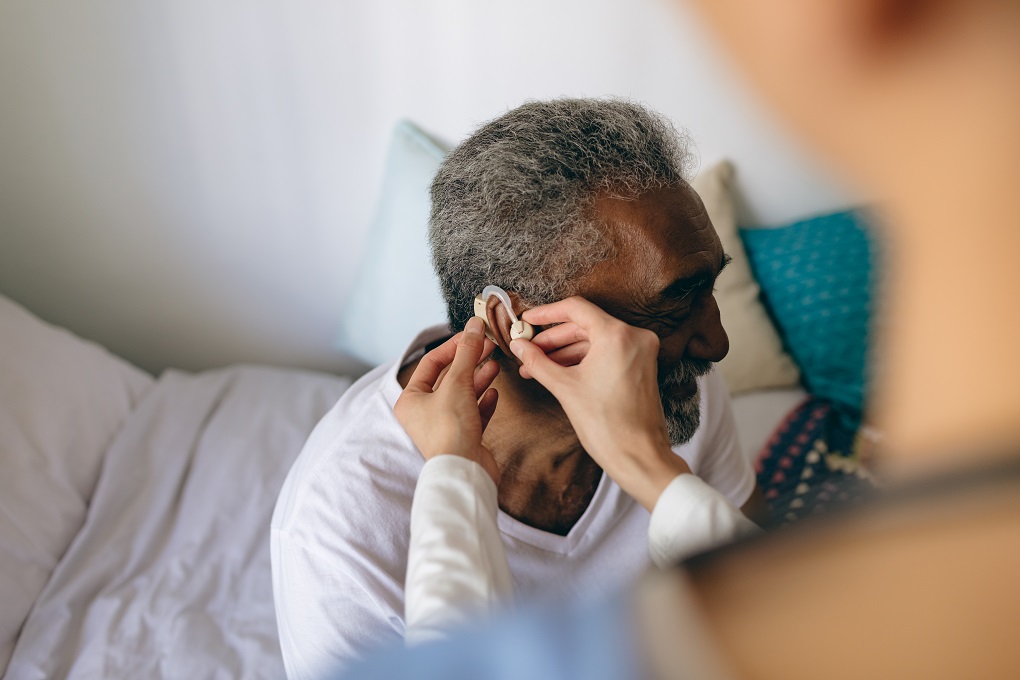 High angle view of Asian female doctor applying hearing aid to senior African-american man ear at retirement home